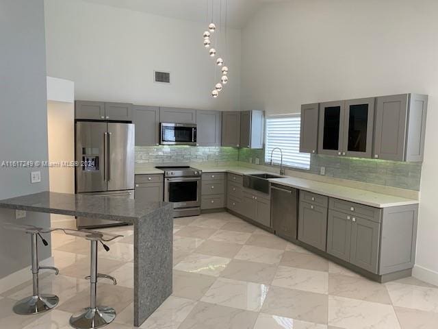 kitchen featuring sink, a kitchen breakfast bar, a towering ceiling, gray cabinets, and appliances with stainless steel finishes