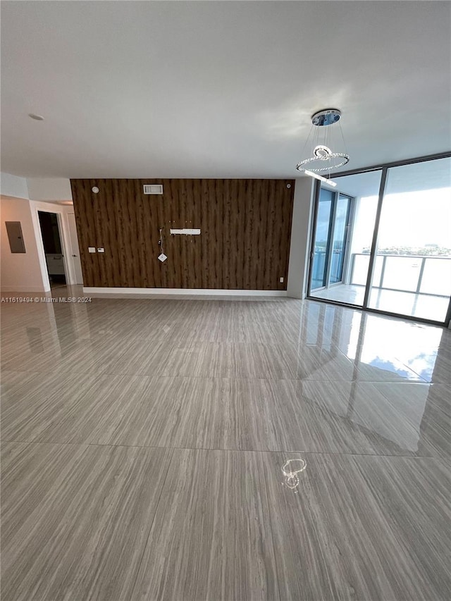 unfurnished living room featuring expansive windows, wooden walls, visible vents, and baseboards