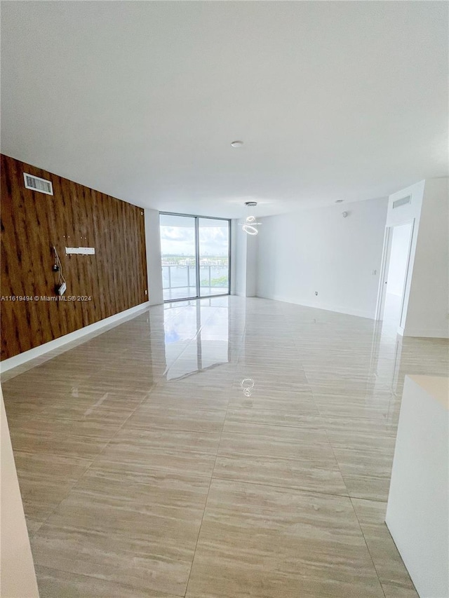 empty room featuring a wall of windows, visible vents, wood walls, and baseboards