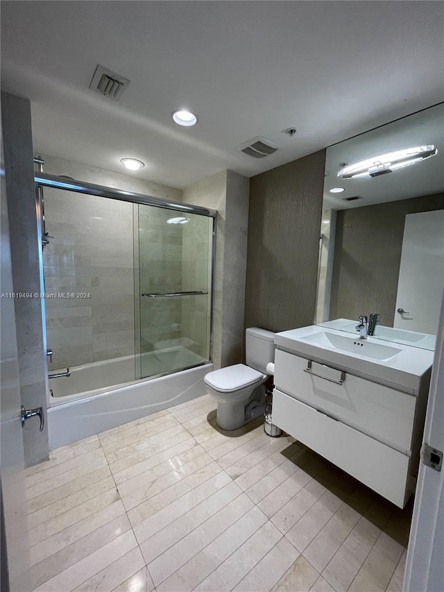 bathroom featuring toilet, visible vents, bath / shower combo with glass door, and vanity