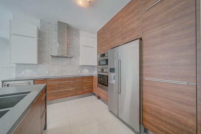 kitchen with tasteful backsplash, stainless steel appliances, wall chimney exhaust hood, sink, and light tile patterned floors