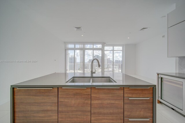 kitchen featuring white cabinetry, expansive windows, beverage cooler, sink, and light tile patterned floors