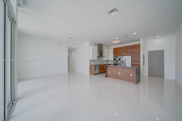 kitchen featuring stainless steel refrigerator with ice dispenser, a center island, light tile patterned floors, and wall chimney exhaust hood