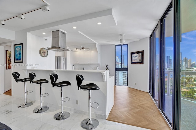 kitchen featuring island range hood, kitchen peninsula, stainless steel fridge, white cabinets, and a breakfast bar