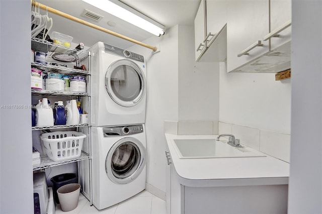 laundry area featuring stacked washer / drying machine, sink, light tile patterned flooring, and cabinets