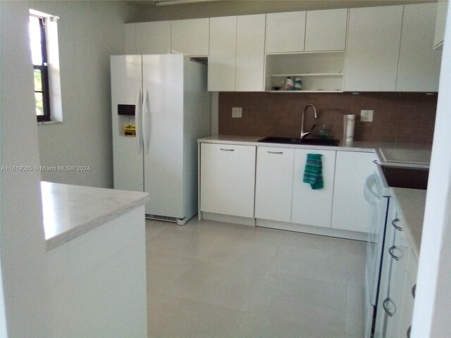 kitchen featuring white fridge with ice dispenser, white cabinetry, light tile patterned floors, and backsplash