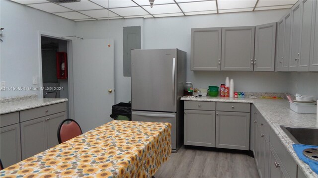 kitchen featuring a paneled ceiling, light wood-type flooring, stainless steel refrigerator, and electric panel