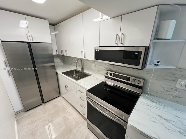 kitchen with white cabinetry, sink, light stone counters, appliances with stainless steel finishes, and light tile patterned floors