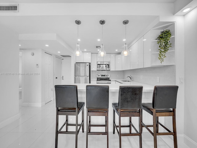 kitchen with white cabinets, appliances with stainless steel finishes, kitchen peninsula, and decorative light fixtures