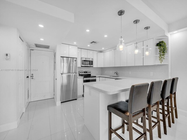 kitchen featuring pendant lighting, white cabinetry, kitchen peninsula, a kitchen bar, and appliances with stainless steel finishes