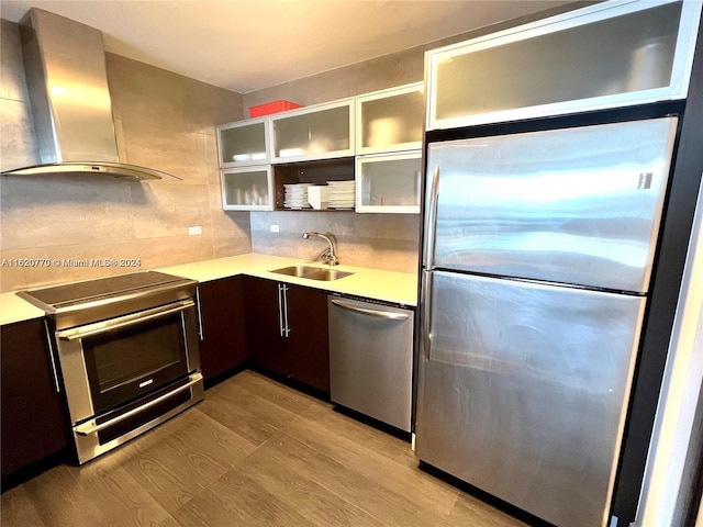 kitchen with light wood-type flooring, wall chimney exhaust hood, dark brown cabinets, stainless steel appliances, and sink