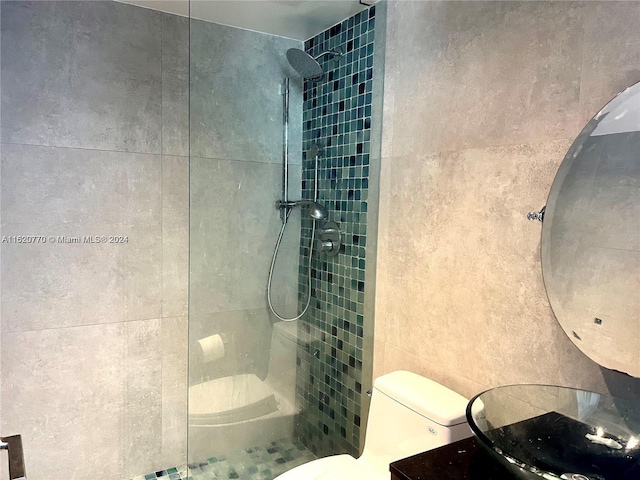 bathroom with toilet, a tile shower, and tile walls