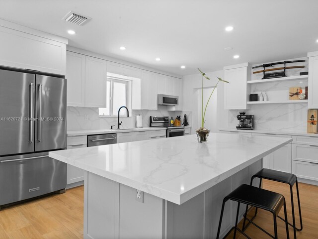 kitchen featuring white cabinets, a center island, stainless steel appliances, and light hardwood / wood-style flooring