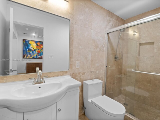 bathroom with tile walls, a shower with shower door, toilet, and vanity