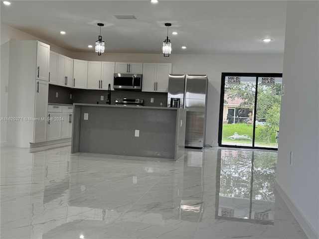 kitchen featuring appliances with stainless steel finishes, decorative light fixtures, white cabinetry, and a center island with sink