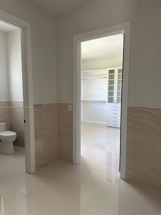 interior space featuring toilet, tile patterned flooring, and tile walls