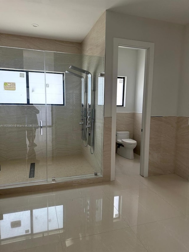 bathroom with a shower with door, tile patterned floors, tile walls, and toilet