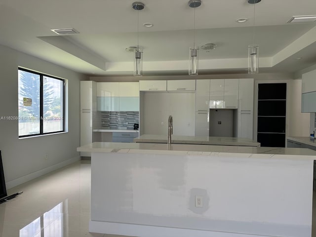 kitchen featuring hanging light fixtures, white cabinetry, decorative backsplash, and a raised ceiling