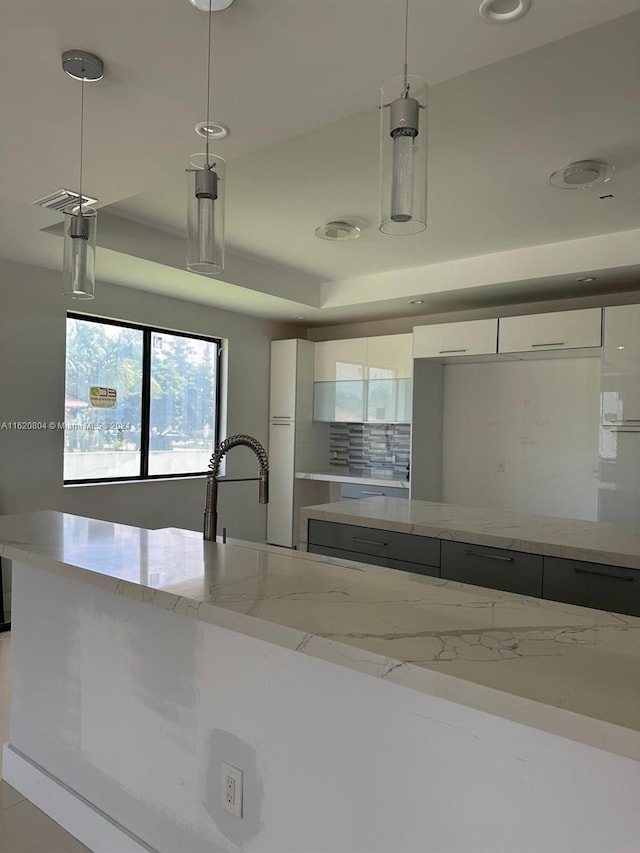 kitchen with white cabinetry, light stone countertops, hanging light fixtures, and tasteful backsplash