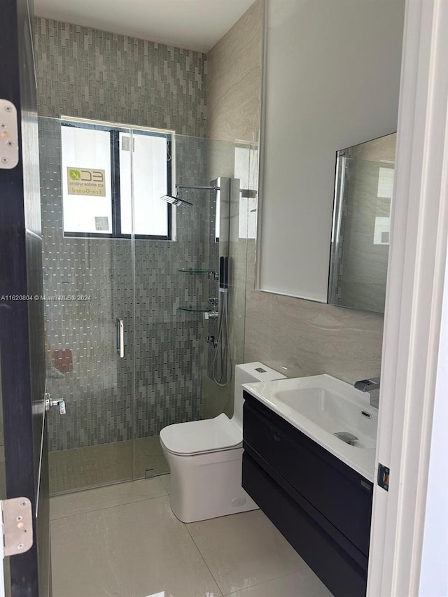 bathroom featuring a shower with shower door, toilet, vanity, tile walls, and tile patterned floors