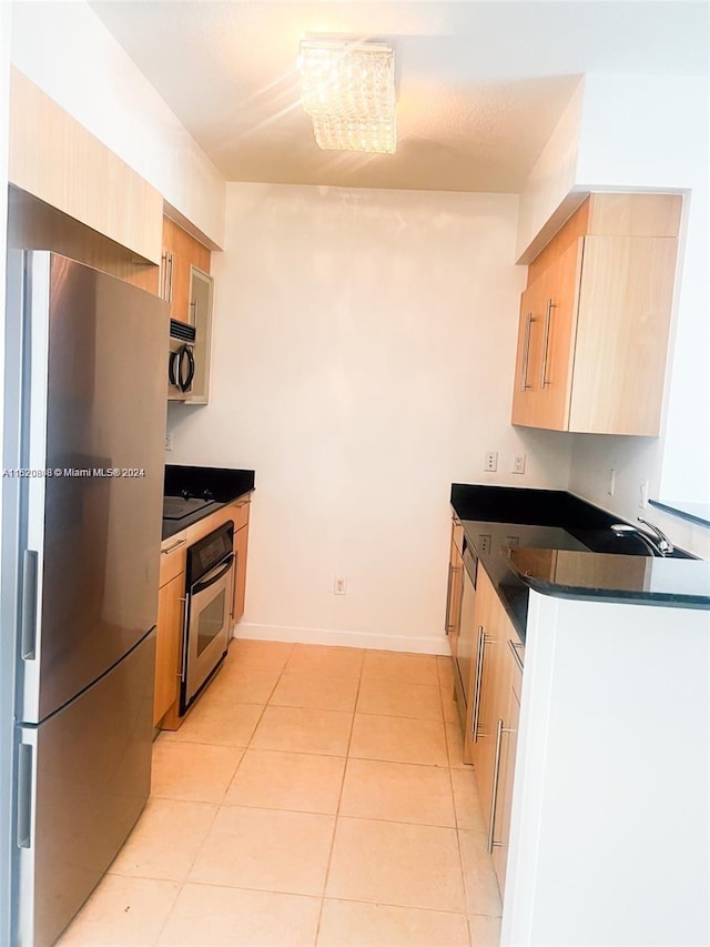 kitchen with light tile patterned flooring, light brown cabinets, appliances with stainless steel finishes, and an inviting chandelier