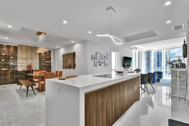 kitchen featuring pendant lighting, a kitchen island, black electric cooktop, light tile patterned flooring, and a tray ceiling