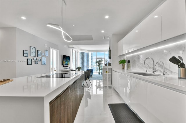 kitchen with sink, tasteful backsplash, decorative light fixtures, black electric stovetop, and white cabinets