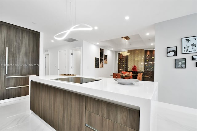 kitchen featuring pendant lighting, black electric stovetop, a tray ceiling, and a kitchen island with sink