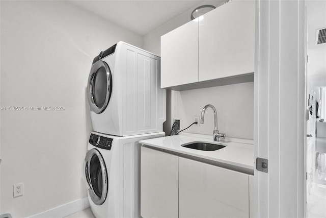 washroom with stacked washer / drying machine, cabinets, and sink