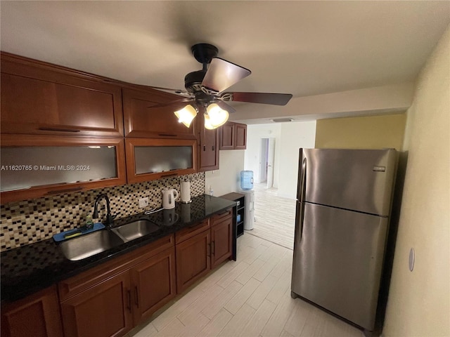 kitchen featuring dark stone countertops, ceiling fan, decorative backsplash, stainless steel fridge, and sink