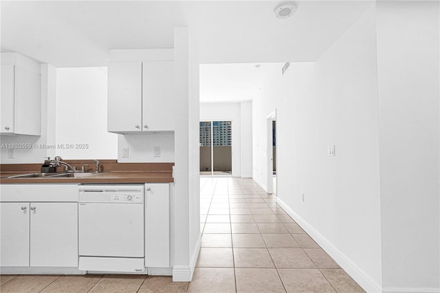 kitchen featuring light tile patterned floors, a sink, baseboards, white cabinets, and dishwasher