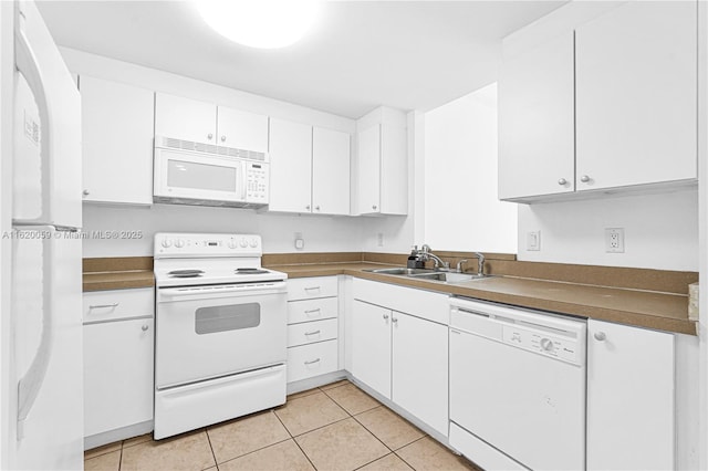 kitchen with light tile patterned floors, white appliances, a sink, white cabinets, and dark countertops