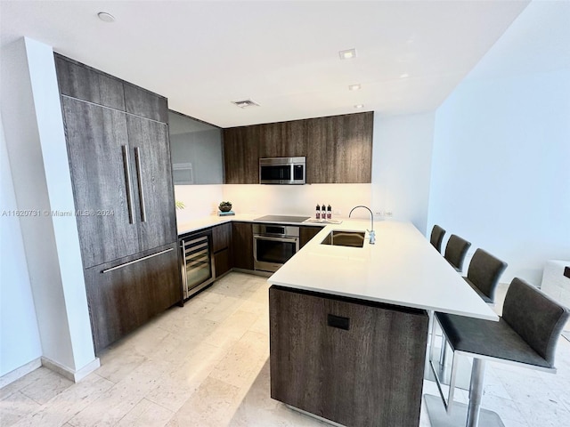 kitchen featuring a kitchen bar, kitchen peninsula, appliances with stainless steel finishes, beverage cooler, and sink