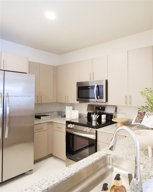 kitchen with cream cabinetry, appliances with stainless steel finishes, light stone counters, and sink