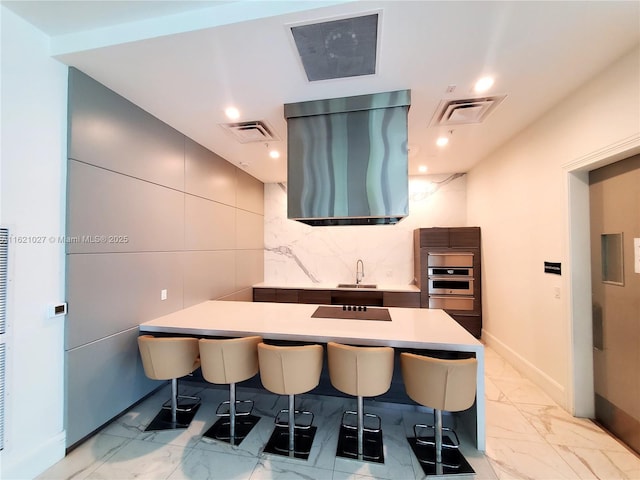 kitchen featuring a kitchen bar, sink, black electric stovetop, oven, and decorative backsplash