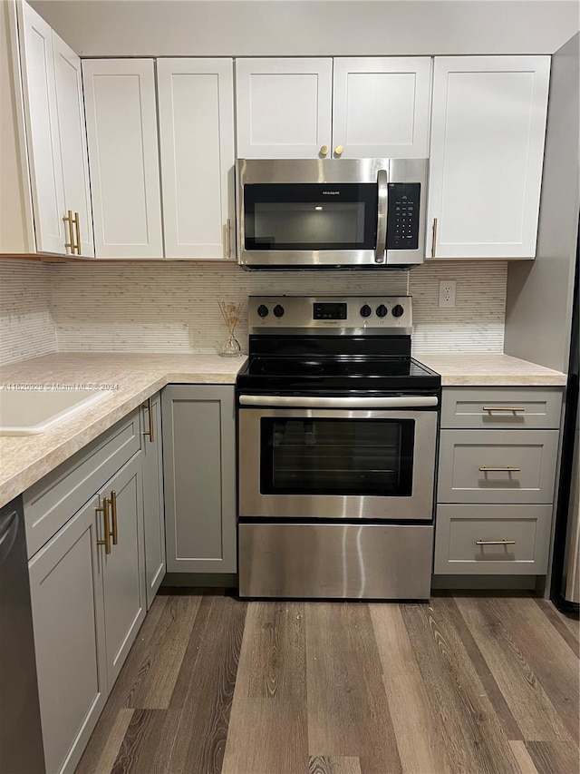 kitchen featuring dark wood-style floors, stainless steel appliances, decorative backsplash, gray cabinetry, and white cabinets