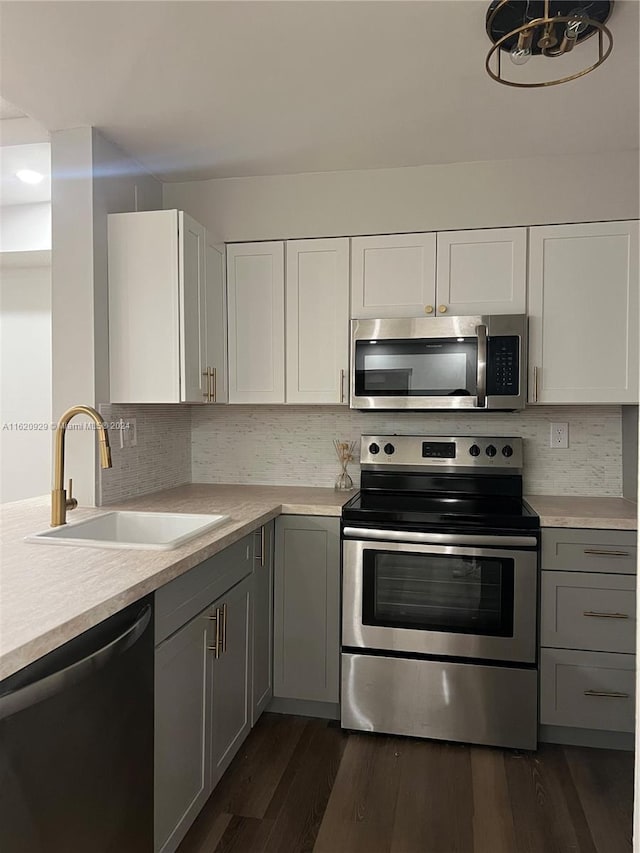 kitchen featuring gray cabinetry, stainless steel appliances, dark wood-style flooring, a sink, and light countertops