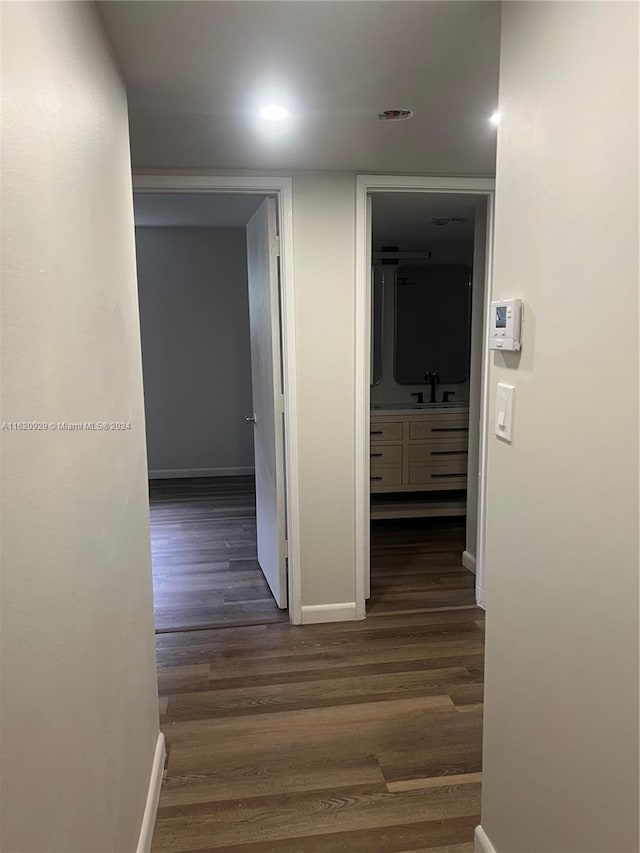 hallway with dark wood-style floors, a sink, and baseboards