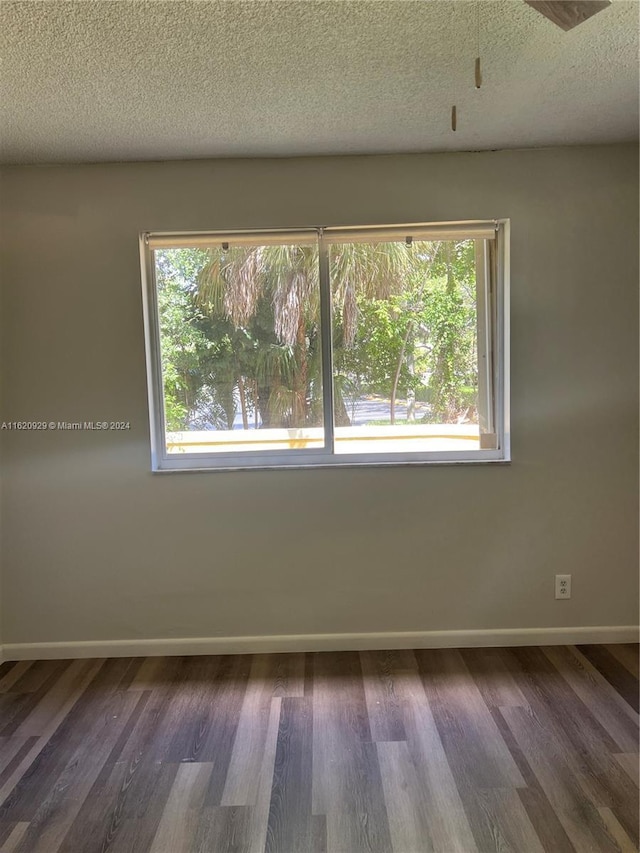 empty room featuring dark wood-style flooring, a textured ceiling, and baseboards