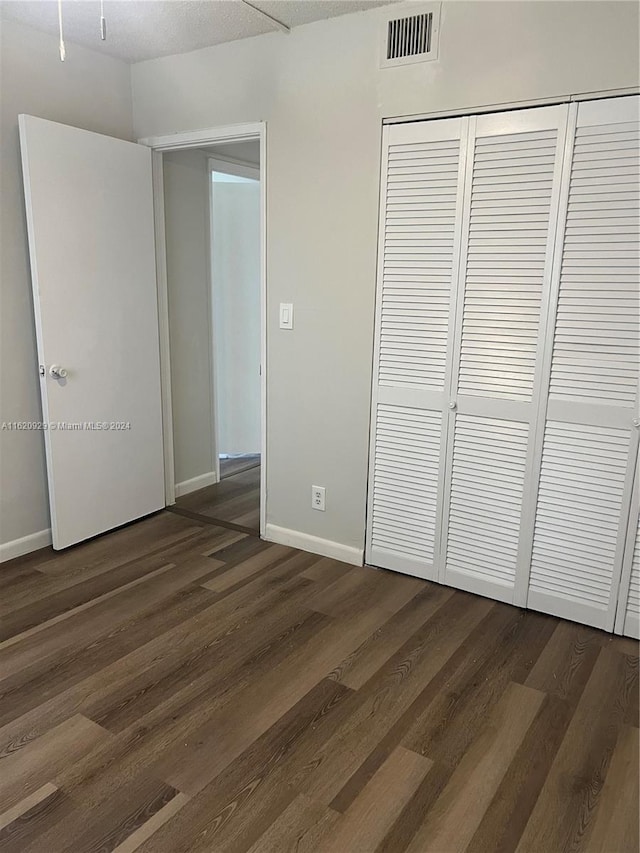 unfurnished bedroom with baseboards, a closet, visible vents, and dark wood-style flooring