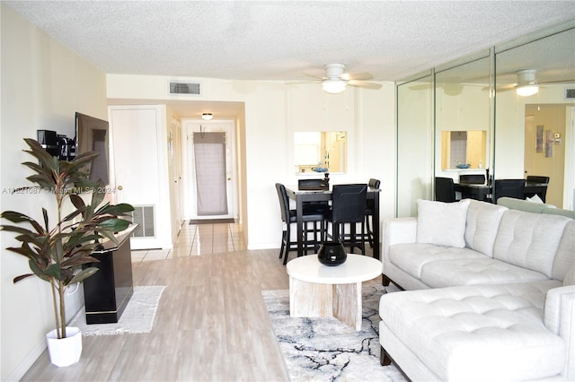 living room with ceiling fan, a textured ceiling, and light wood-type flooring