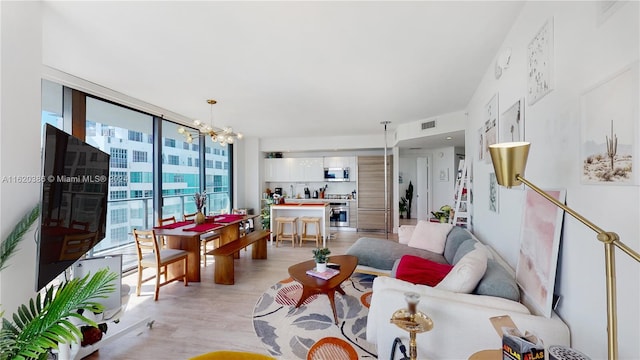 living room with light wood-type flooring, a notable chandelier, and a wall of windows