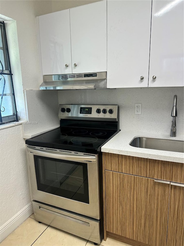 kitchen featuring white cabinets, light tile patterned flooring, stainless steel electric range oven, and sink