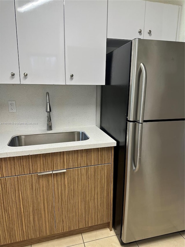 kitchen with sink, white cabinets, stainless steel refrigerator, backsplash, and light tile patterned floors