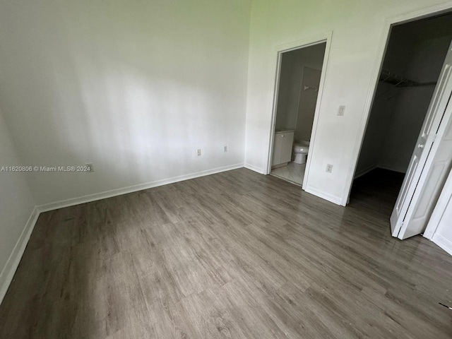 unfurnished bedroom featuring ensuite bath, dark wood-type flooring, a walk in closet, and a closet