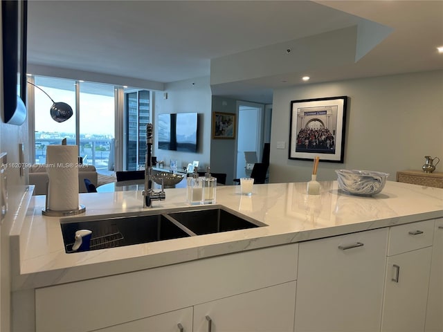 kitchen with expansive windows, open floor plan, white cabinets, a sink, and light stone countertops