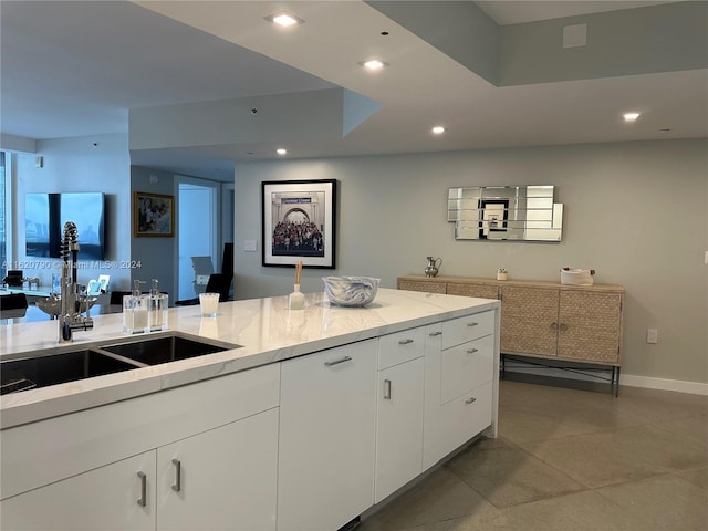 kitchen with baseboards, light stone countertops, white cabinetry, a sink, and recessed lighting