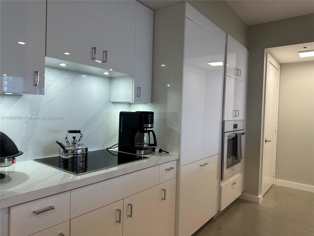 kitchen with oven, white cabinetry, tasteful backsplash, and black electric stovetop