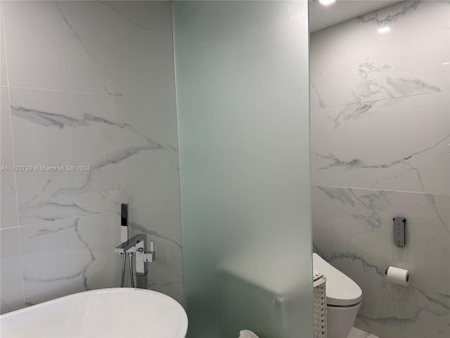 bathroom featuring stone wall, marble finish floor, a soaking tub, and toilet