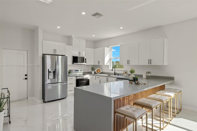 kitchen with white cabinetry, sink, stainless steel appliances, a kitchen breakfast bar, and kitchen peninsula